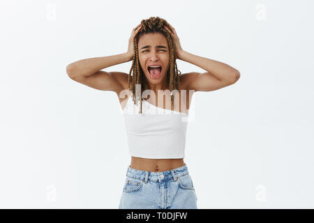 Ragazza andando folle. Ritratto di farsi prendere dal panico emotivo di carnagione scura donna reazione esagerata urlando dal panico e shock tenendo le mani sul dreadlocks urlare Foto Stock