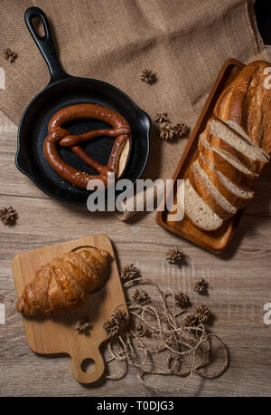 Cornetti freschi e salatini con baguette di pane, posti su un vassoio e un tagliere di legno, posto su una tavola di legno dalla vista dall'alto. Foto Stock