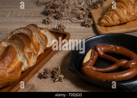 Cornetti freschi e salatini con baguette di pane posti su un vassoio e un tagliere di legno posto su una tavola di legno Foto Stock