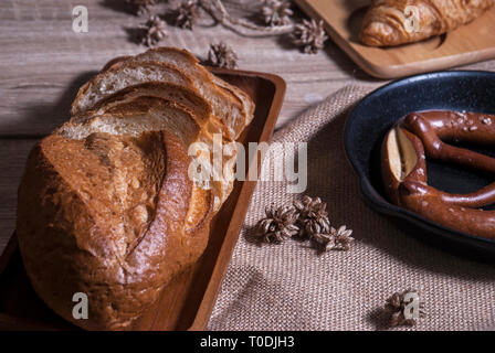 Cornetti freschi e salatini con baguette di pane posti su un vassoio e un tagliere di legno posto su una tavola di legno Foto Stock