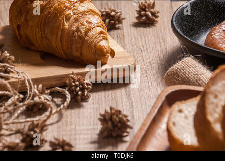 Cornetti freschi sono posti su di un tagliere di legno su una tavola di legno, insieme con altri tipi di pane per la colazione. Foto Stock