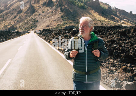 Adulto di età senior uomo a camminare con zaino in una lunga strada di montagna godendo le vacanze alternative di viaggio e di vivere uno stile di vita avventura - ret Foto Stock