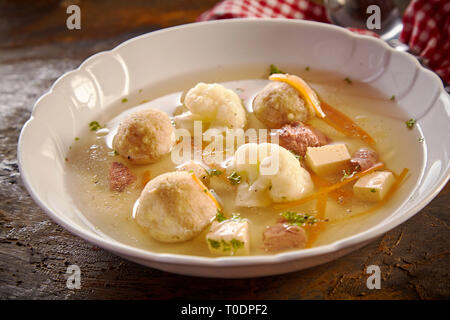 Molla di gourmet di brodo con il tedesco midollo osseo gnocchi di patate, fresche e cavolfiore tagliato in julienne carote guarnita con erbe in un angolo basso vista ravvicinata Foto Stock