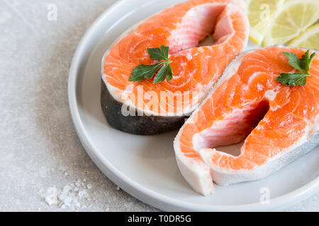 Pesce fresco salmone fresco bistecche con limone, spezie e sale in una piastra di luce. Foto Stock