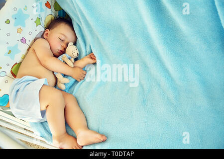 Bambino con un peluche orso. ragazzino che giace in una mangiatoia su una coperta di blu Foto Stock