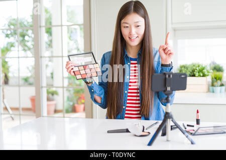 Bella asiatica influencer donna la registrazione compongono tutorial utilizzando la fotocamera dello smartphone sorpreso con un'idea o domanda puntare il dito con la faccia felice Foto Stock