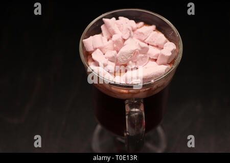 Bevanda calda in un bicchiere di vetro con rosa marshmallows e scatola bianca con una copertura trasparente a forma di cuore con i cookie Foto Stock