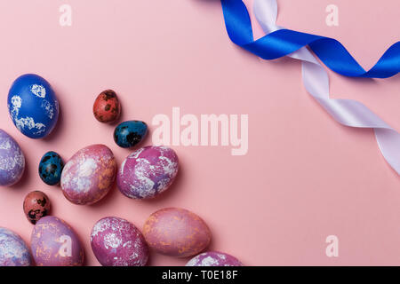 Gioioso della Pasqua uova colorate di bianco e blu con nastro su sfondo rosa. Spazio per il testo, concetto di sfondo di Pasqua Foto Stock
