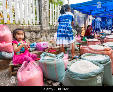 Bambina giocando accanto a madre al mercato del riso in stallo, mattina street market alimentare, Luang Prabang, Laos, SE Asia Foto Stock