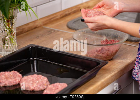 Materie carni macinate in esili donna con le mani in mano. Ragazza costolette di cottura sulla cucina moderna Foto Stock