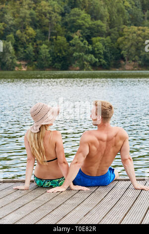 Coppia giovane seduto su di un molo di legno in un lago balneabile in vacanza in estate Foto Stock