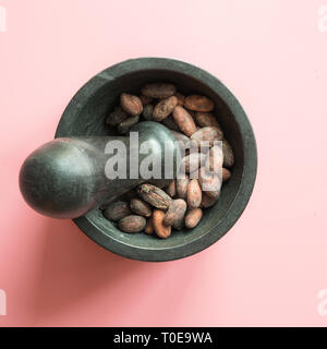 Concetto di fave di cacao in ciotole su sfondo rosa. Foto Stock