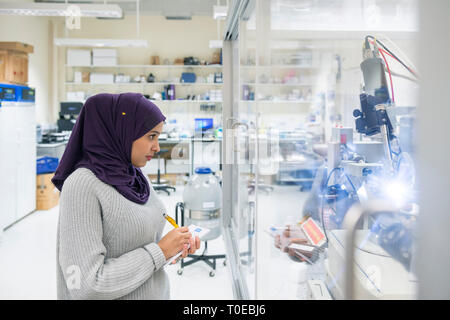 Una donna musulmana utilizza le attrezzature scientifiche in un laboratorio di ricerca, presso la University of Sussex indossando un tradizionale hijab. Foto Stock