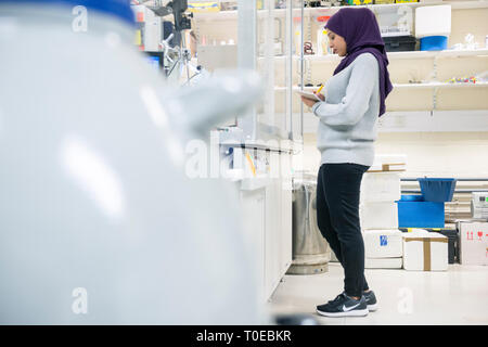 Una donna musulmana utilizza le attrezzature scientifiche in un laboratorio di ricerca, presso la University of Sussex indossando un tradizionale hijab. Foto Stock