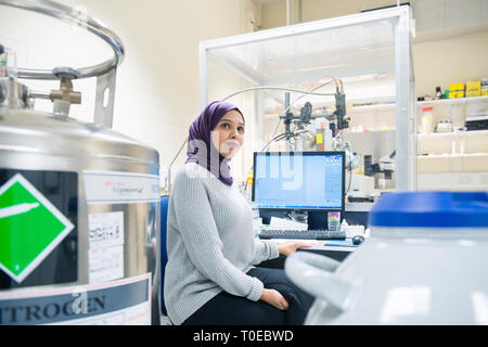 Una donna musulmana utilizza le attrezzature scientifiche in un laboratorio di ricerca, presso la University of Sussex indossando un tradizionale hijab. Foto Stock