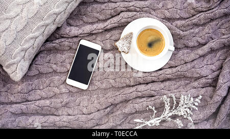 White tazza di caffè con i cookie nella forma di abete e telefono bianco fiore sul cuscino grigio e calda lana rosa grigio plaid. Tessile lavorato a maglia con motivo a treccia. Autunno Inverno concetto di comfort Foto Stock