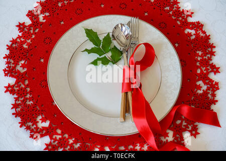 Natale e Anno Nuovo Holiday Tabella di impostazione del luogo con il vischio holly foglia. Vista superiore, rosso lana e sfondo bianco. Vacanze invernali concept Foto Stock