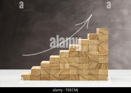 Concetto di crescita. Grafico con gradini in legno su uno sfondo grigio con la freccia disegnata. Foto Stock