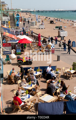 La gente seduta al di fuori del caffè lungo la passeggiata sul lungomare di Brighton, Sussex, Inghilterra. Foto Stock