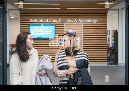 Due giovani studenti asiatici che camminando in e fuori della porta di un moderno palazzo universitario Foto Stock