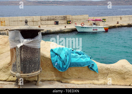 Telo da spiaggia accanto al cestino decorativo può, in barca e il mare in background Foto Stock