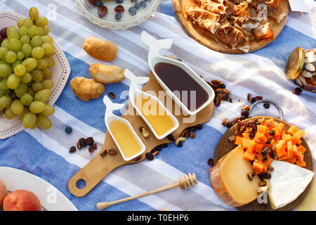 Set di tre sauceboats bianco con il dolce miele sul vassoio in legno a picnic food lay out dello sfondo. Foto Stock