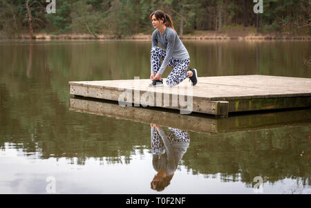 Runner donna sua legatura lacci delle scarpe per preparare a correre da un lago Foto Stock