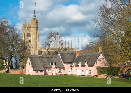 Cottage con il tetto di paglia dipinta in Suffolk rosa con Santa Maria Vergine la Chiesa sul verde villaggio. Cavendish, Suffolk, East Anglia, UK. Foto Stock