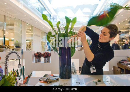 Un fiorista disponendo dei fiori in un centro commerciale di spedizione. Al di sopra è un lucernario che danno molta luce naturale. La donna è focalizzato e concentrato. Foto Stock