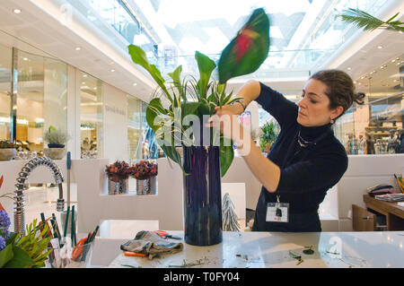 Un fiorista disponendo dei fiori in un centro commerciale di spedizione. Al di sopra è un lucernario che danno molta luce naturale. La donna è focalizzato e concentrato. Foto Stock