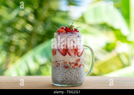 Latte di mandorle budino di Chia con rosso fresco Fragole, goji bacche e fiocchi di avena in un vasetto di vetro mug. Vegan materie prima colazione. Semi di Chia e fresco tagliato fr Foto Stock