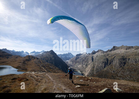 Pilota di parapendio decolla con il suo parapendio a decollare e volare nella valle nelle Alpi Svizzere. Foto Stock