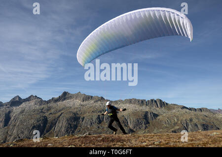 Pilota di parapendio decolla con il suo parapendio a decollare e volare nella valle nelle Alpi Svizzere Foto Stock