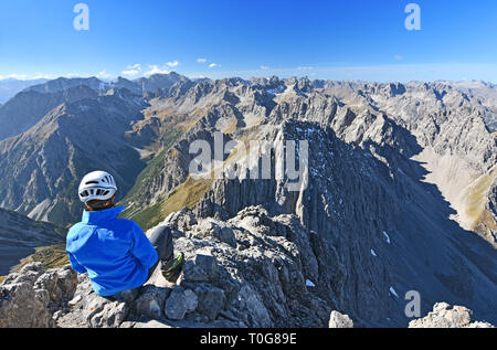 Scalatore femmina seduto in cima a una montagna (Lechtal Alpi, Tirolo, Austria). Paesaggio alpino con mounrains rocciosi e cielo blu. Foto Stock