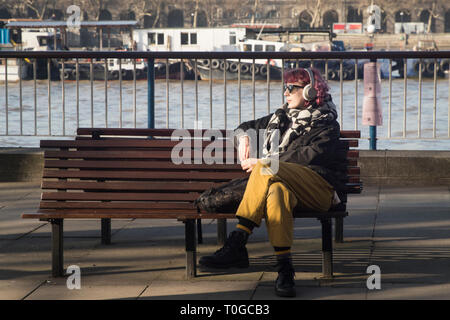 Londra - 15 febbraio 2019: Ragazza nelle cuffie si siede sul banco e ascolta la musica al di fuori del Royal Festival Hall a South Bank Foto Stock