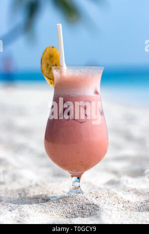 Cocktail di frutta e una fetta di banana sulla sommità e paglia sulla sabbia a una spiaggia delle Maldive. Foto Stock