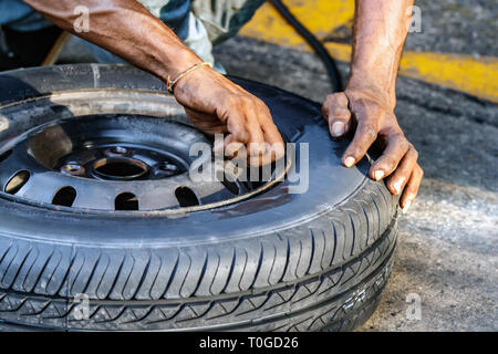 Un pneumatico repairman è che fissano le tazze di polvere sulla valvola del pneumatico all'aperto in una stazione di rifornimento a Galle, Sri Lanka. Foto Stock