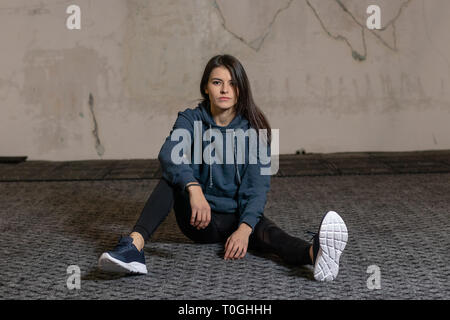 La ragazza si siede sul pavimento in palestra Foto Stock