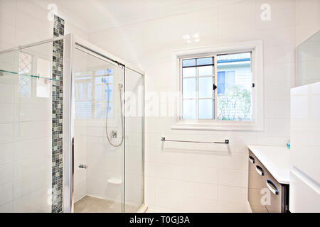Bianco moderno bagno interno con box doccia in vetro e montato a parete vanità cercando di una piccola finestra che si affaccia sul vicini Foto Stock