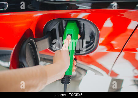 Il veicolo elettrico stazione di carica. Close-up di donna mano carica di un auto elettrica con la potenza di alimentazione del cavo collegato alla presa di corrente. Eco-friendly auto concept Foto Stock