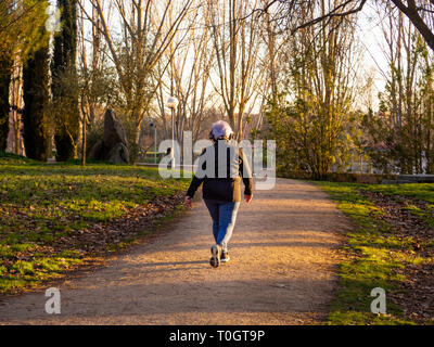 Un senior donna con i capelli bianchi per ascoltare musica con le cuffie a camminare in un parco urbano Foto Stock