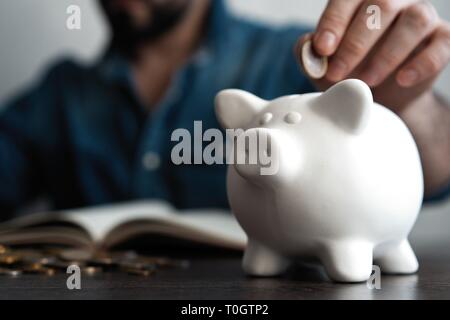 Uomo di mettere moneta nel salvadanaio. Risparmio di denaro concept Foto Stock