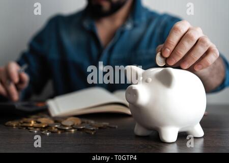 Uomo di mettere moneta nel salvadanaio. Risparmio di denaro concept Foto Stock