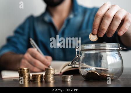 Contabilità aziendale con risparmio di denaro con la mano di mettere le monete in caraffa di vetro finanziario concept Foto Stock