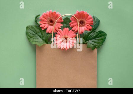 Coral gerbera daisy fiori in craft papper shopping bag sul libro verde sullo sfondo, Primavera vendita Concetto di immagine con copy-spazio Foto Stock
