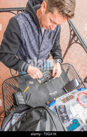 Un iPhone repairman imposta shop sul marciapiede patio di un locale coffee shop con un segno in casa pubblicità 'Riparazione iPhone' e il suo numero di telefono. H Foto Stock