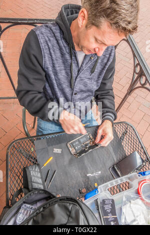 Un iPhone repairman imposta shop sul marciapiede patio di un locale coffee shop con un segno in casa pubblicità 'Riparazione iPhone' e il suo numero di telefono. H Foto Stock