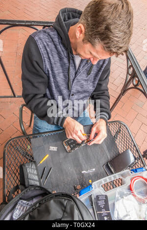 Un iPhone repairman imposta shop sul marciapiede patio di un locale coffee shop con un segno in casa pubblicità 'Riparazione iPhone' e il suo numero di telefono. H Foto Stock