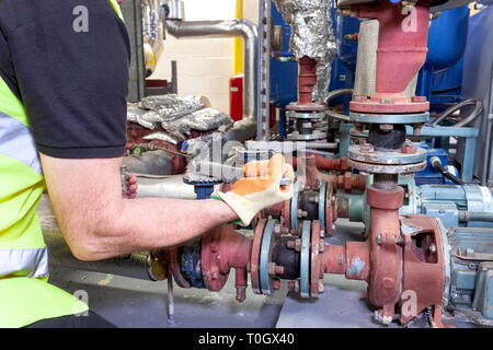 Ingegnere meccanico in un giubbotto di sicurezza con fasce catarifrangenti lavorando su un set di pompa in un locale caldaia Foto Stock