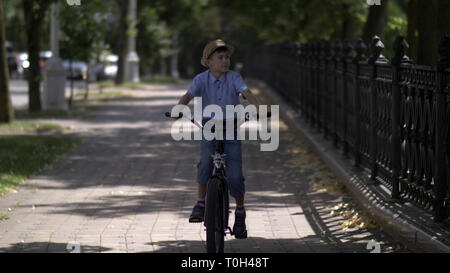 Felice ragazzo in un cappello vanno in bicicletta in un parco cittadino, divertirsi Foto Stock